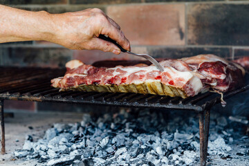 The hand of a mature man doing a barbecue. He is prodding the meat with a fork. - obrazy, fototapety, plakaty
