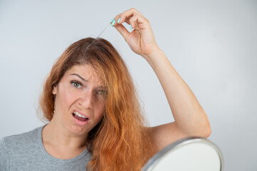 Fototapeta premium Caucasian woman finds gray hair and removes it with tweezers. Signs of aging.