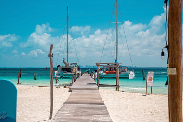 Cancun, Mexico. May 30, 2021. Wooden pier leading from sand into sea with moored yachts or sailboat on water surface