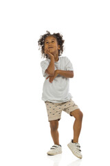 Small black boy in shorts and shirt is looking up and thinking. Full length, isolated.