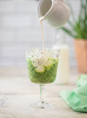 Cold Matcha green tea with ice cube and milk. Healthy eating concept. Pouring milk into a glass of green tea.