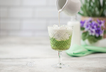 Cold Matcha green tea with ice cube and milk. Healthy eating concept. Pouring milk into a glass of green tea.