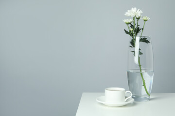 Vase with chrysanthemums and cup of coffee on white table