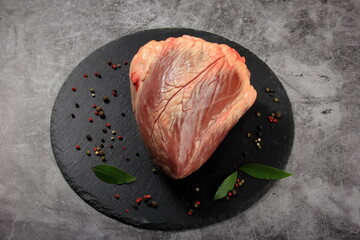 Beef raw heart on a black stone background with salt, green leaves and spices. 