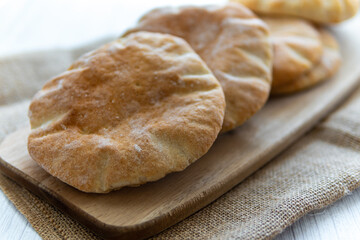 Selective focus on pita bread on a wooden board, hot from the oven. Homemade, freshly baked gluten-free flatbread or pitta. Fluffy, round bread to be stuffed with food. Rustic cloth, white background.