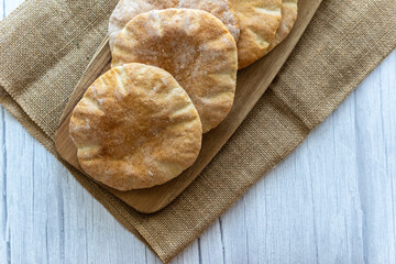 Pita bread on a wooden board, hot from the oven. Homemade, freshly baked gluten-free flatbread or pitta. Fluffy, round bread that can be stuffed with food. Rustic cloth and white wooden background.
