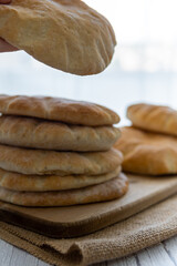 Hand taking a pita bread from a pile on a wooden board, hot from the oven. Homemade, freshly baked gluten-free flatbread or pitta. Fluffy, round bread that can be stuffed with food. White background.
