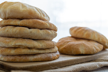 Stack of pita bread on a wooden board, hot from the oven. Homemade, freshly baked gluten-free flatbread or pitta. Fluffy, round bread that can be stuffed with food. Rustic cloth and white background.