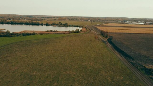 slow low flying drone antenna over the lake , corn autumn field and dirt road in cloudy weather.