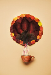 Colorful hot air balloon made of autumn leaves flying with a cup coffee on a beige background, flat lay. Creative concept
