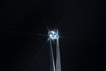 Diamond selective focus held in metal jeweller tweezers, brilliant stone cut with star shape light...