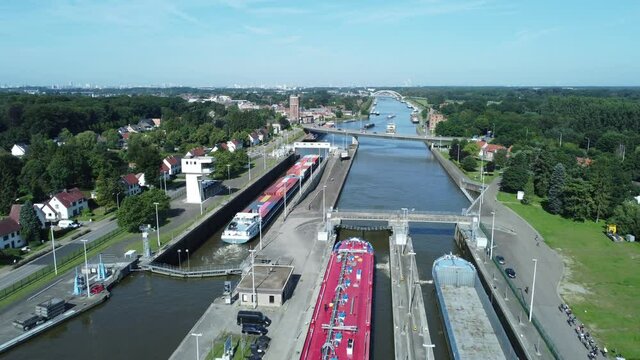Flying over lock with boats and barges at Albert canal and group of cyclists cycling on the road next to the water in Wijnegem sluis near Antwerp. Aerial drone shot.