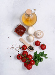 Olive oil in a glass decanter, cherry tomatoes, champignons and peppers lie on a bright table. Top view