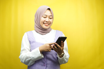 Beautiful young asian muslim woman smiling confidently holding smartphone isolated on yellow background, advertising concept