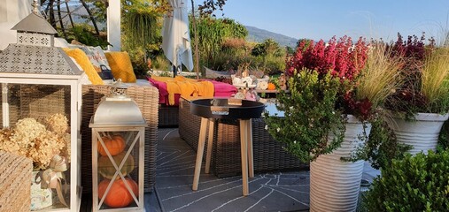 A big terrace with a comfortable leisure sofa with cushions, a table and a string swing in a green garden during sunny vacation.