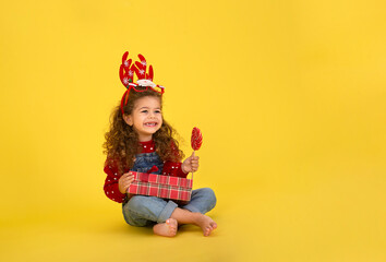 Portrait of happy little  girl Christmas  holding present box and looking at camera on yellow background
