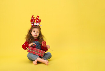 Portrait of happy little  girl Christmas  holding present box and looking at camera on yellow background
