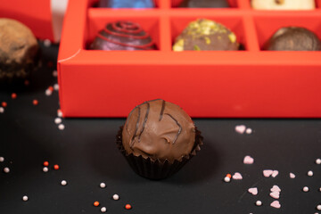 Various handmade chocolate truffle candies in a red box on a dark background. Close up view.