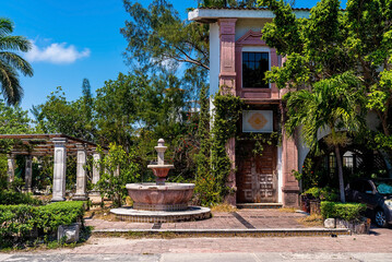 Old dry fountain next to a spanish style building at roadside with window and closed door, ivy...