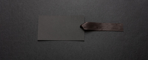 Black price tag blank mockup with satin ribbon isolated against black background,
