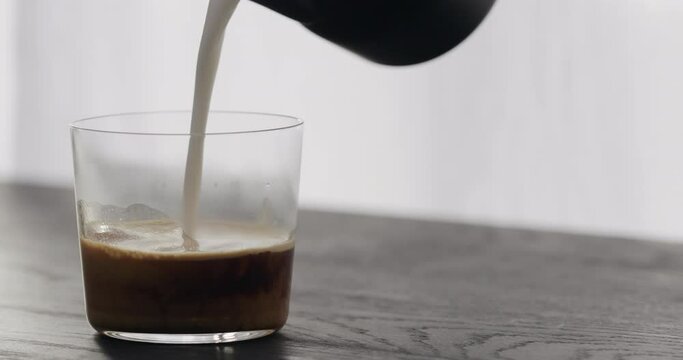 Slow motion making cappuccino in tumbler glass on black aok table