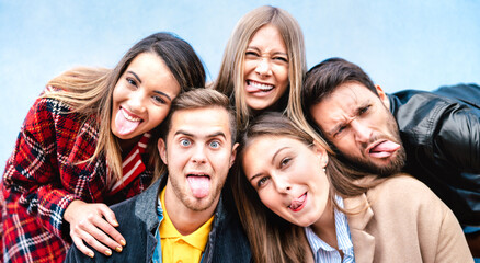 Multicultural milenial guys and girls taking selfie sticking out tongue with happy faces - Crazy life style concept with young students friends having fun together outdoors - Bright vivid filter