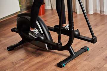 Legs of woman training on elliptical cross trainer in living room at home