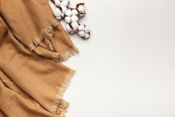 Beige cashmere scarf with a branch of cotton on a light gray background. Flat lay, top view, copy space