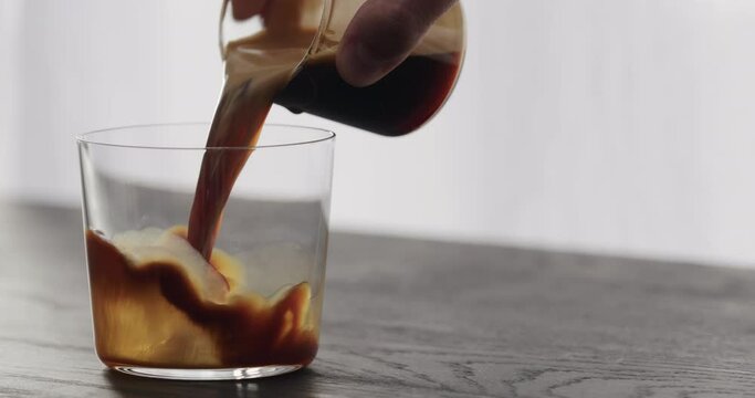 Slow motion pour espresso in tumbler glass on black aok table