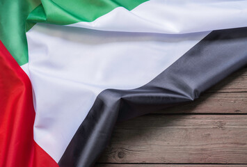The flag of the United Arab Emirates lies on a brown wooden background with space for text or image.