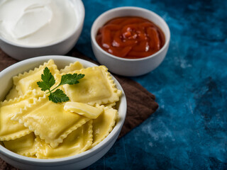 A portion of Italian ravioli, garnished with a mint leaf and two sauces - tomato and sour cream on a beautiful marble blue background. Restaurant, cafe, hotel, menu design.