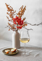 Glass of white wine,  apple, decorative bouquet of mountain ash branches on a table in a bright...