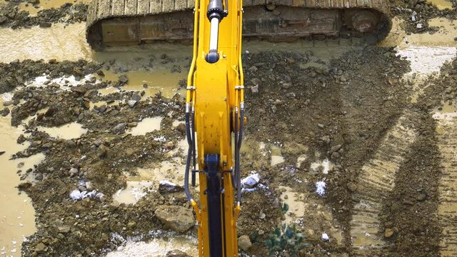 Digger working deep in the mud and water clearing out the bottom of construction basement. Bucket scoops water out of a ditch on the site for the construction the building after heavy rain