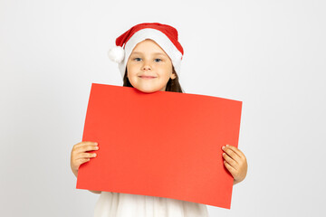 close-up portrait of beautiful, six-year-old girl in Santa Claus hat holding red empty poster isolated on white background. 