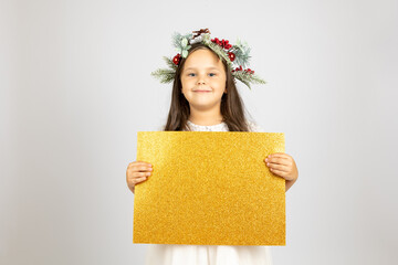 close-up portrait of charming, smiling girl in Christmas wreath holding golden, shiny blank banner isolated on white background. 