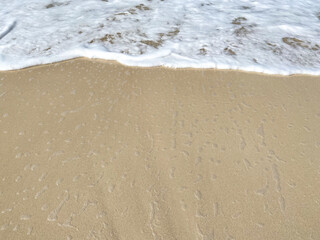 White sea wave foam crashing on clear wet sand on sea shore