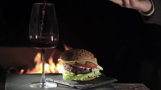 Hamburger on the background of fire. They put a glass of wine on a stone tray.