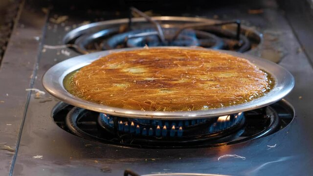 Chef cooking a traditional Turkish dessert named Kunefe on hot iron plate.