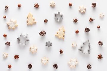 Christmas background. The pattern is made of Christmas cookies, nuts, cones, cookie cutters and anise stars on a white background.