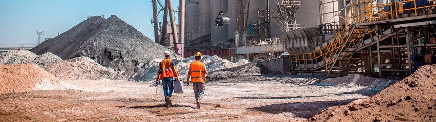 People are working in the industry. Modern technologies work at a cement plant. Technological work on the production of cement. Working atmosphere with copy space. Heaps of sand and soil raw materials - obrazy, fototapety, plakaty