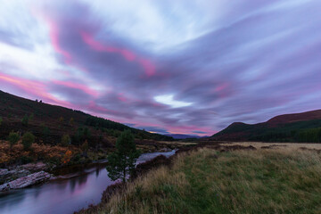 Glen Feshie with river with red illuminated clouds in evening time in Cairngorms National Park,...