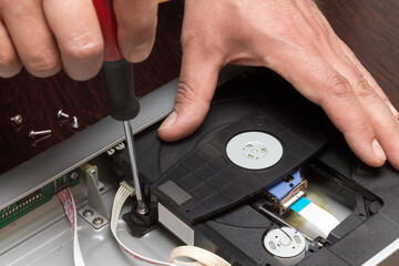 A man holds a screwdriver and unscrews the mechanism of the DVD player for repair, Adobe RGB color...