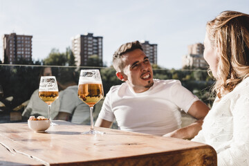 happy hispanic couple drinking beer in outdoor pub on sunny day, focus on the beer