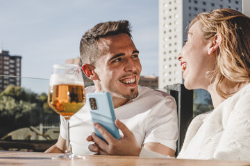 happy couple drinking beer and using smartphone on a sunny day