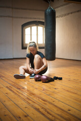 Woman getting ready for training. Young woman in black sport clothes sitting on floor tying laces. Sport, healthy lifestyle, boxing concept