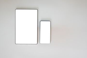 Smartphone and tablet screens are white on a white background, suitable for use for mackup. Copy space is available.