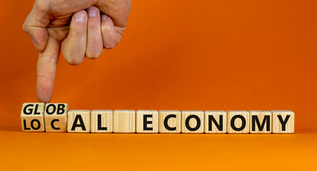 Local or global economy symbol. Businessman turns wooden cubes and changes words local economy to global economy. Beautiful orange background. Business, local or global economy concept. Copy space.