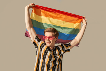 Caucasian man proudly holding the LGBT flag and looking away while posing