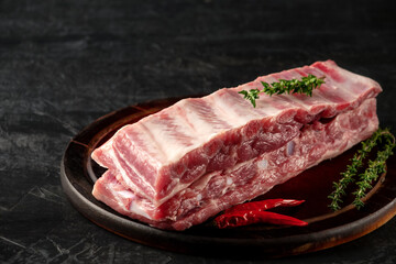 Raw pork ribs with spices and thyme on a dark wooden background