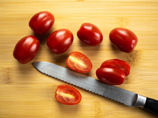 Pigeon heart cherry tomatoes on a bamboo board with a knife, background. Flat lay, top view.